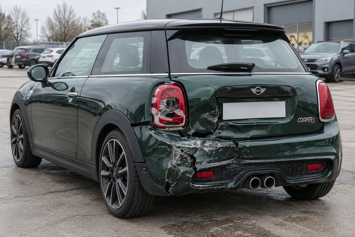 Dunkelgrüner MINI Cooper S, Baujahr 2018, von hinten links: eingedrückte Heckklappe, beschädigter Stoßfänger und zerbrochene Rückleuchte